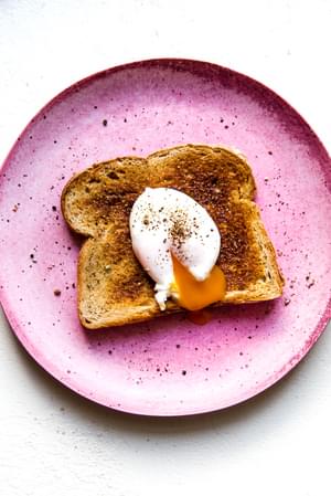 Pink plate with a piece of toast and a poached egg with salt and pepper