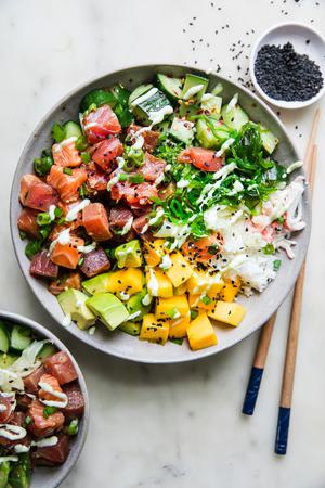 A poke bowl featuring a base of seasoned rice, topped with tuna salmon, mango, cucumber salad, avocado & citrus wasabi sauce
