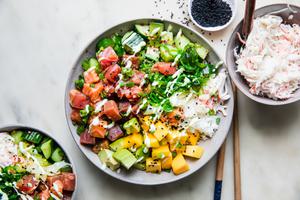 A poke bowl featuring a base of seasoned rice, topped with tuna salmon, mango, cucumber salad, avocado & citrus wasabi sauce