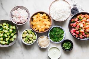 A vibrant assortment of poke bowl ingredients arranged in bowls: tuna and salmon, mango, cucumber, avocado & seasoned rice