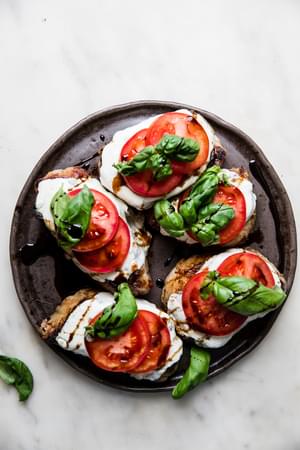grilled pork chops topped with mozzarella, tomato slices, basil and balsamic glaze on a platter