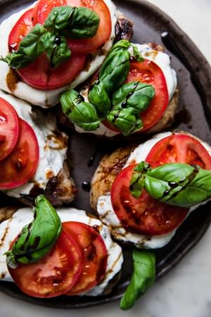 grilled pork chops topped with mozzarella, tomato slices, basil and balsamic glaze on a platter