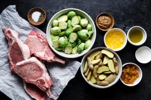 ingredients for pork chop sheet pan dinner, potatoes in a bowl, Brussels sprouts, salt, pepper, whole grain mustard apricot