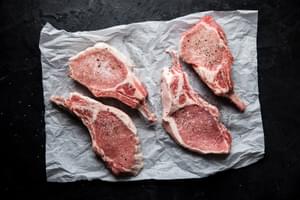 4 bone in pork chops with salt and pepper on parchment paper
