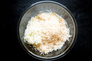 eggs, flour, salt, pepper, onions and potatoes in a mixing bowl for homemade potato pancakes