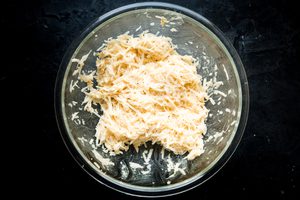 eggs, flour, salt, pepper, onions and potatoes in a mixing bowl for latkes recipe