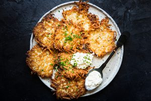 homemade latkes on a plate topped with a dollop of sour cream
