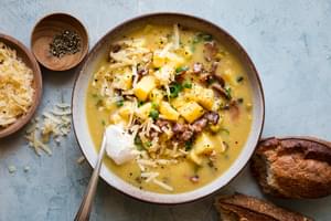 a bowl of potato and corn chowder in a bowl topped with shredded cheese and a dollop of sour cream surrounded by toppings