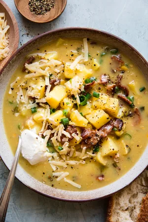 Potato and Corn chowder in a bowl topped with shredded cheese and a dollop of sour cream along side crusty bread