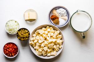 queso dip ingredients in bowls on the counter American cheese, tomatoes, whole milk, green chiles, butter, spices, and onions