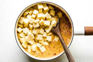 american cheese being stirred into butter, onions, tomatoes, chiles, cornstarch and whole milk in a sauce pan