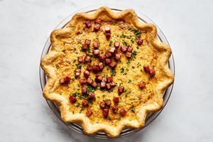 Quiche Lorraine in a pie pan made with eggs, cream, ham, brown sugar, nutmeg, spices and Gruyère topped with chives