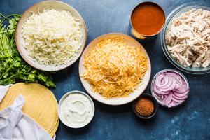 shredded chicken, cheese, taco seasoning, sour cream, enchilada sauce, red onion and cilantro in bowls on the counter