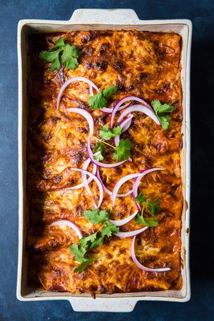 homemade red chicken enchiladas topped with cilantro and red onion