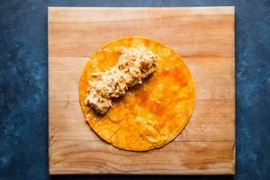 a corn tortilla covered in enchilada sauce with enchilada filling sitting on top on a bread board