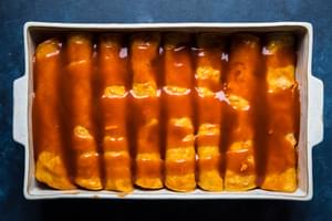 red chicken enchiladas rolled in a baking dish and covered with enchilada sauce