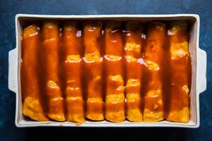 red chicken enchiladas rolled in a baking dish and covered with enchilada sauce