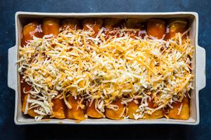 homemade red chicken enchiladas topped with shredded cheese ready to go in the oven