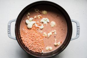 coconut oil, garlic, onion, spices, crushed tomatoes, coconut milk, cauliflower and red lentils in a pot for red lentil soup