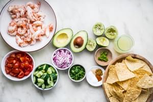 cooked shrimp in a bowl with avocado, red onion, tomatoes, cucumber, lime juice, cilantro, avocado and tortilla chips