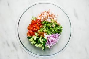 a bowl with cucumber, red onion, cilantro, shrimp, tomatoes and jalapeño