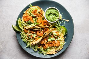shrimp tacos topped with cabbage slaw and avocado crema served with lime wedges