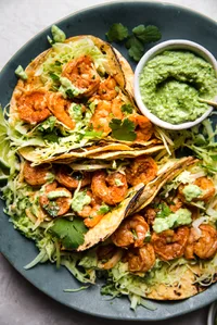shrimp tacos topped with cabbage slaw and avocado crema served with lime wedges