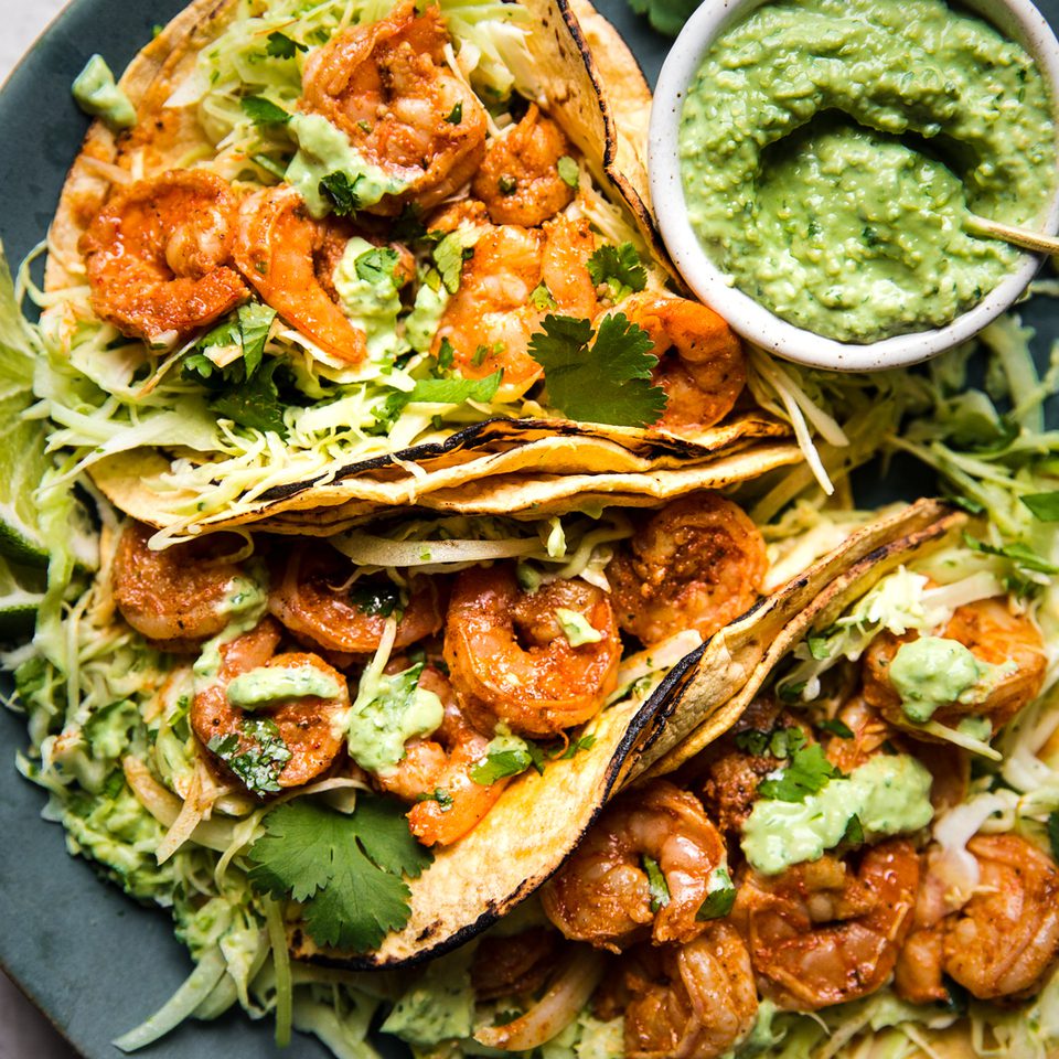 shrimp tacos topped with cabbage slaw and avocado crema served with lime wedges