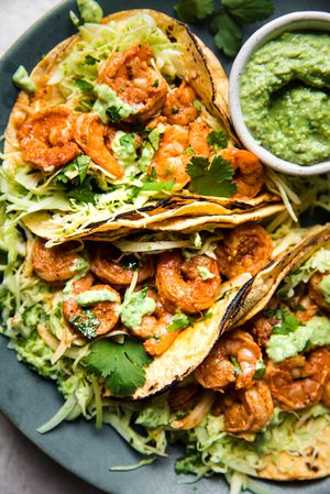 shrimp tacos topped with cabbage slaw and avocado crema served with lime wedges