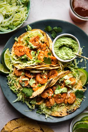 shrimp tacos topped with cabbage slaw and avocado crema served with lime wedges