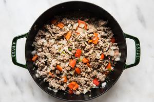 ground beef and pork, onion, peppers, jalapeño and garlic being cooked in a pot