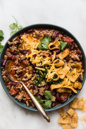 homemade chili recipe in a bowl topped with cheddar cheese and green onion