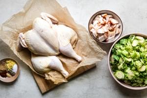 spatchcocked whole chicken on parchment paper surrounded by bowls of shaved Brussels sprouts, bacon and spices