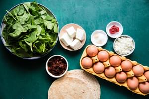 eggs, whole wheat tortillas, spinach, feta and sun dried tomatoes in prep bowls to make Starbucks spinach feta wraps