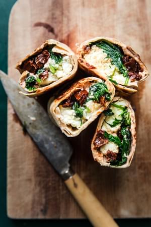 spinach feta wraps filled with tomato cream cheese, sun dried tomatoes, feta & scrambled egg whites sliced on a cutting board