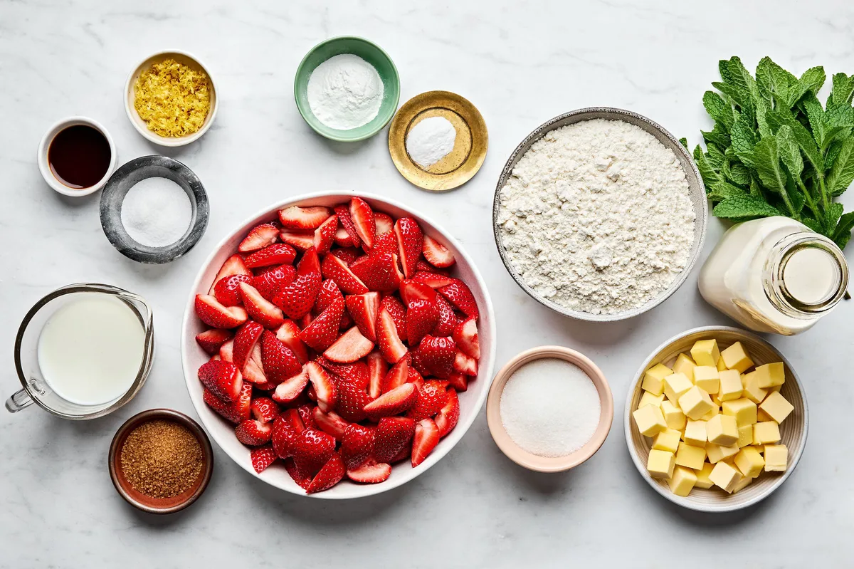 Ingredients for strawberry shortcake laid out on a countertop: fresh strawberries, flour, sugar, butter and buttermilk