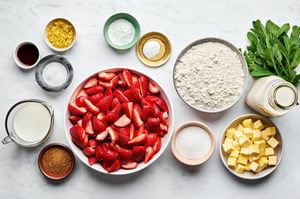 Ingredients for strawberry shortcake laid out on a countertop: fresh strawberries, flour, sugar, butter and buttermilk