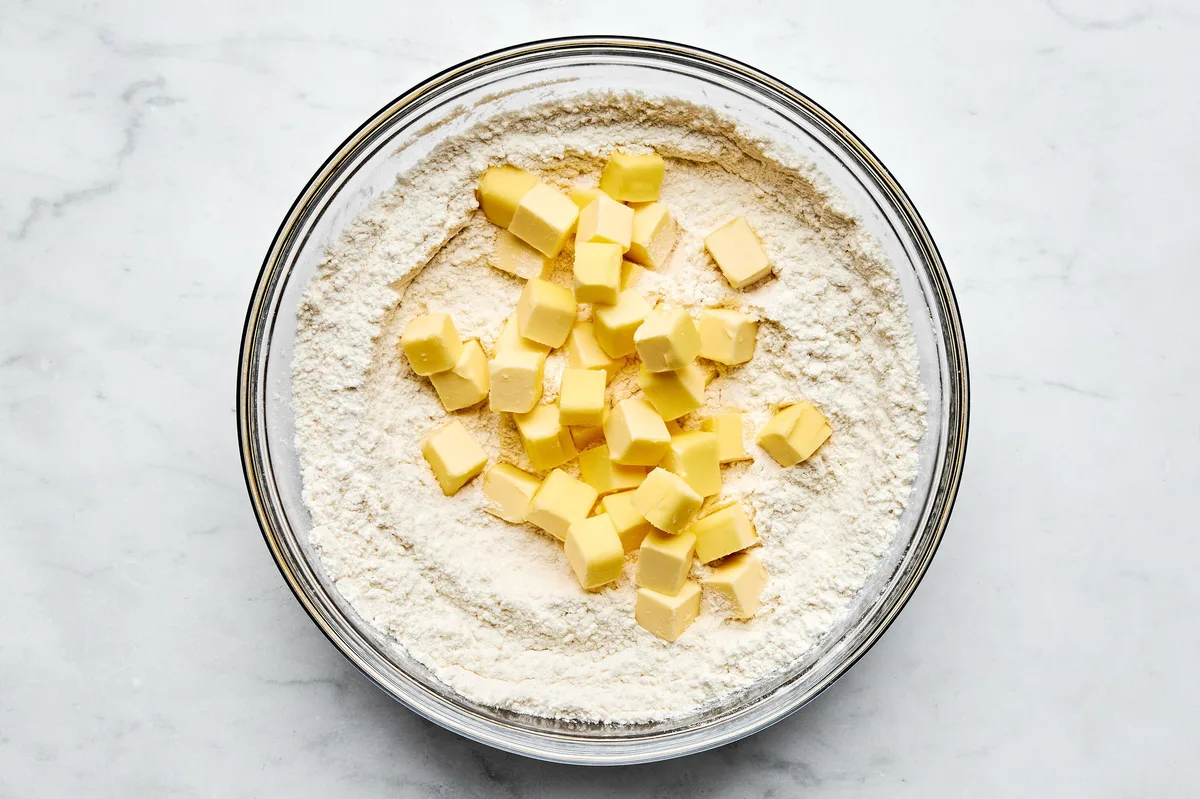 cold chopped butter being added to a bowl of flour, sugar, baking powder, baking soda and salt