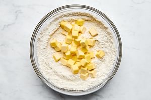 cold chopped butter being added to a bowl of  flour, sugar, baking powder, baking soda and salt