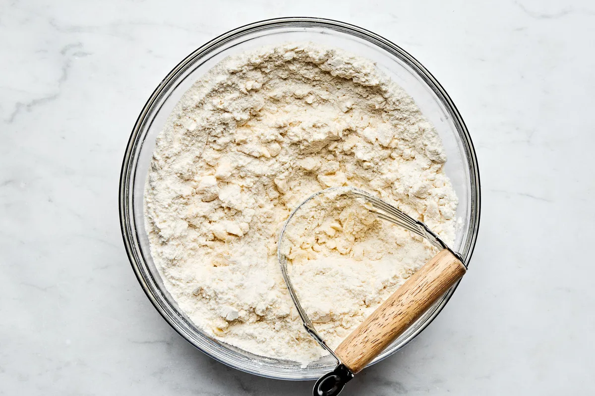 cold butter being cut into a bowl of flour, sugar, baking powder, baking soda and salt to make shortcake biscuits