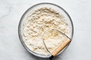 cold butter being cut into a bowl of flour, sugar, baking powder, baking soda and salt to make shortcake biscuits