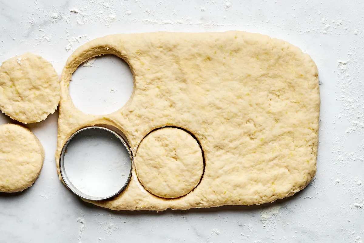 Round biscuit shapes being cut out of homemade dough on a floured surface