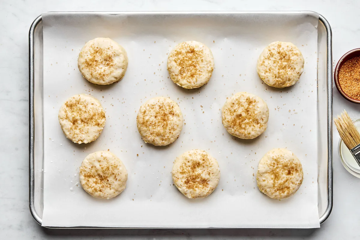 Unbaked homemade biscuits arranged on a parchment-lined baking sheet, sprinkled with raw sugar, ready to go into the oven