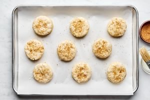 Unbaked homemade biscuits arranged on a parchment-lined baking sheet, sprinkled with raw sugar, ready to go into the oven