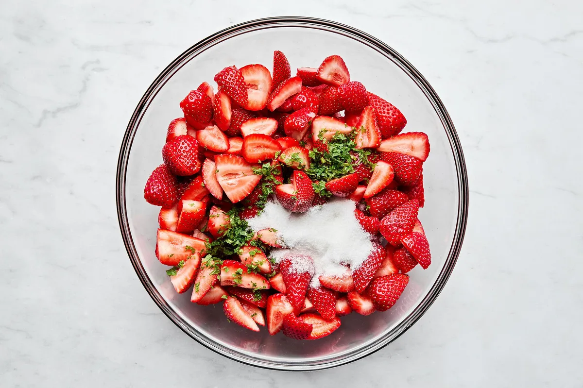 a bowl of fresh, sliced strawberries being tossed with sugar and mint for strawberry shortcake