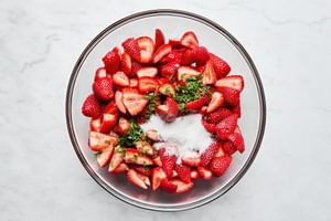 a bowl of fresh, sliced strawberries being tossed with sugar and mint for strawberry shortcake