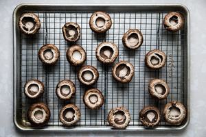 cremini mushrooms with stems removed on a cooling rack inside of a baking sheet