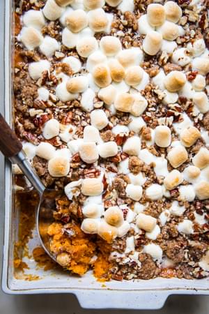 baked Homemade Sweet Potato Casserole with Marshmallows and Pecan Streusel in a baking dish being scooped with a wooden spoon