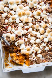 baked Homemade Sweet Potato Casserole with Marshmallows and Pecan Streusel in a baking dish being scooped with a wooden spoon