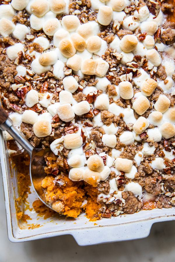 baked Homemade Sweet Potato Casserole with Marshmallows and Pecan Streusel in a baking dish being scooped with a wooden spoon